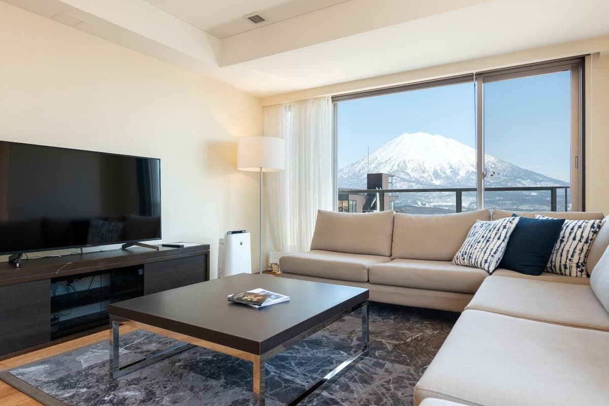 Una sala de estar moderna con un televisor de pantalla plana, un sofá, una mesa de centro y un ventanal con vistas a la montaña.