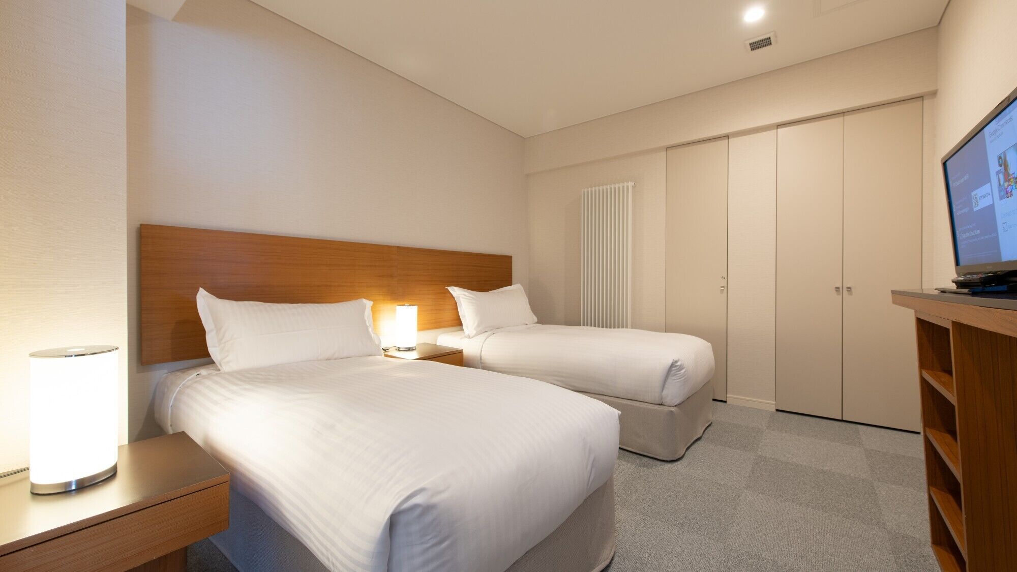 A hotel room with two beds, a TV, a desk, and a wardrobe.