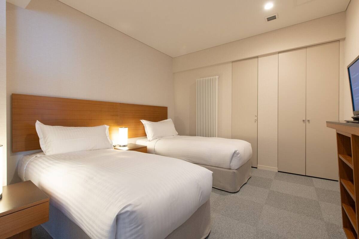 Habitación de hotel con dos camas, televisión, escritorio y armario.