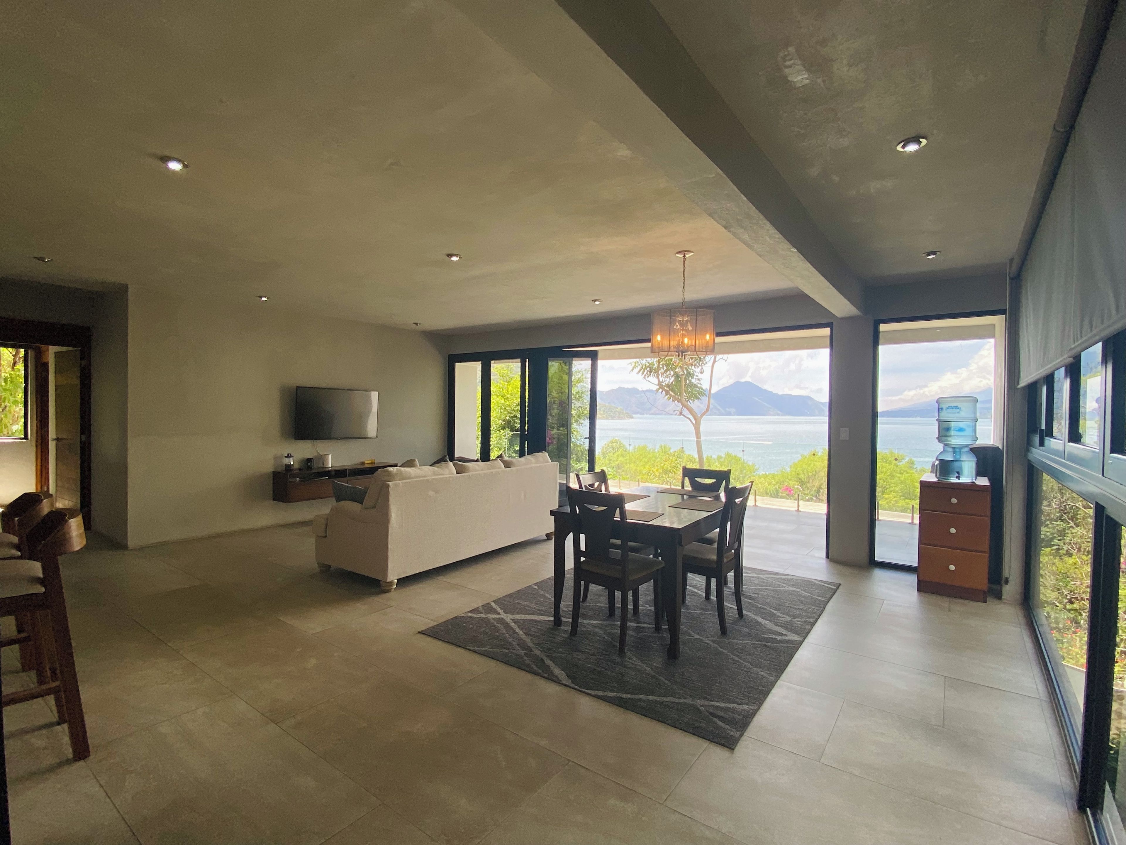Um espaço de estar moderno com área de jantar, sofá, TV e vista para o exterior.