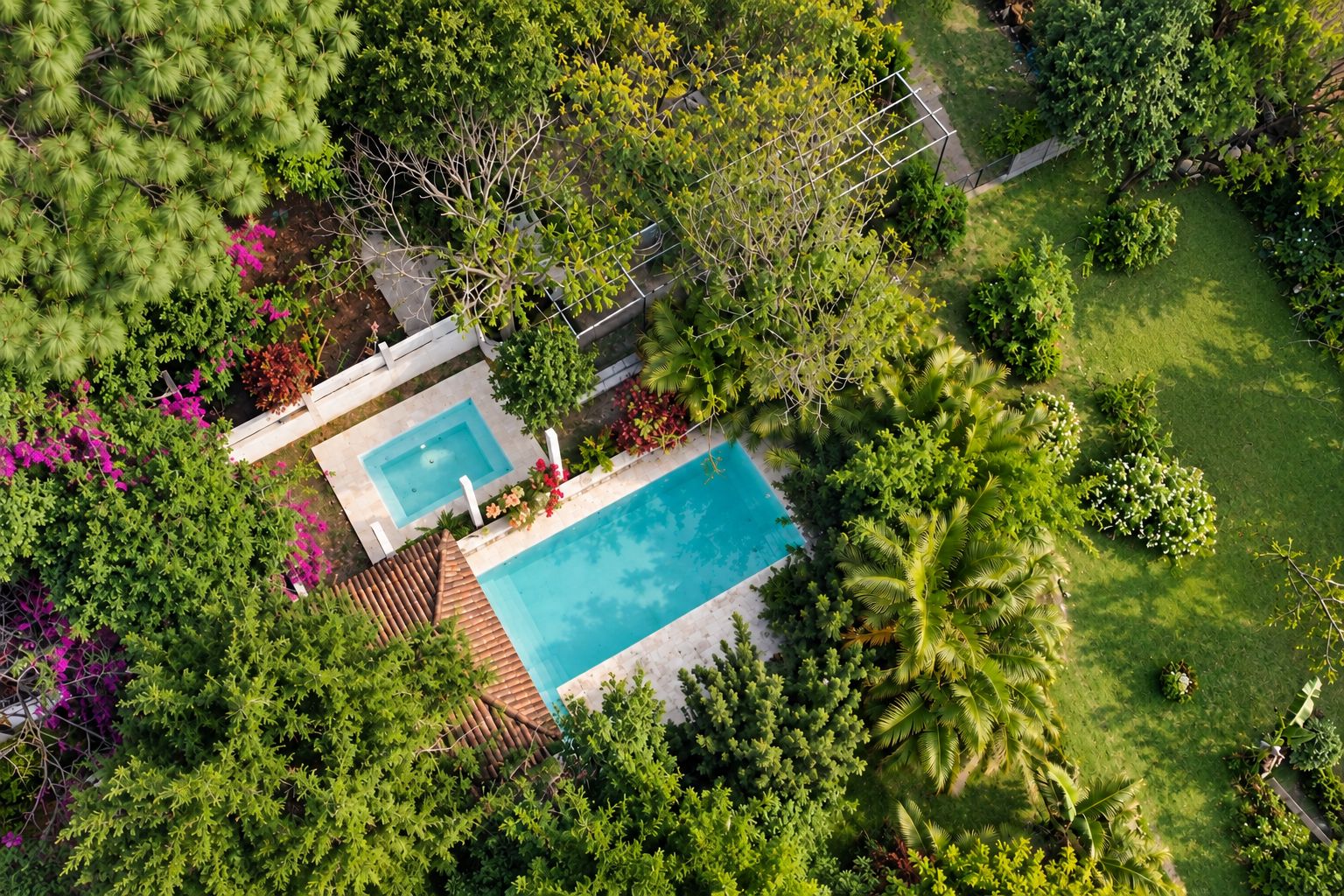 Vista aérea de una propiedad residencial con piscina rodeada de exuberante vegetación y un césped bien cuidado.