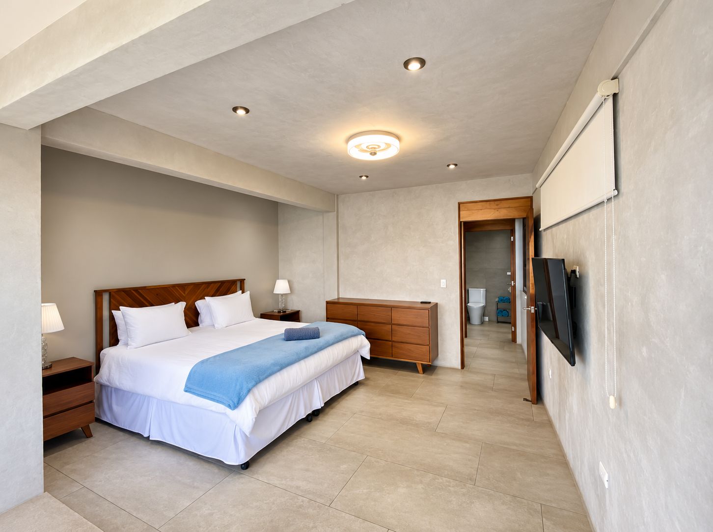 Een hotelkamer met een bed, nachtkastjes, een kaptafel, een televisie en een badkamer die door een open deur zichtbaar is.