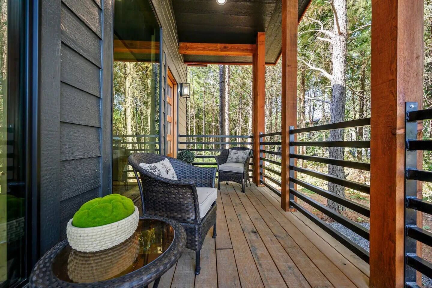 A wooden deck with wicker furniture and a green cushion, surrounded by trees.
