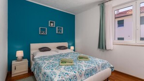Un dormitorio con una pared de acento color turquesa, una cama blanca y una ventana con cortinas.