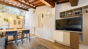 A modern kitchen with wooden flooring, a dining area with chairs, a built-in TV, and a window with a view. - Giglio Celeste apartment in Florence by Mmega (Firenze)