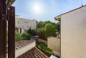 A view through a window with a tiled roof, a white building, and greenery in the background.