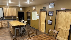 Une cuisine avec des meubles en bois, un grand îlot central avec des tabourets, une table à manger avec des chaises et un panneau indiquant « East Glacier Park VFO ».