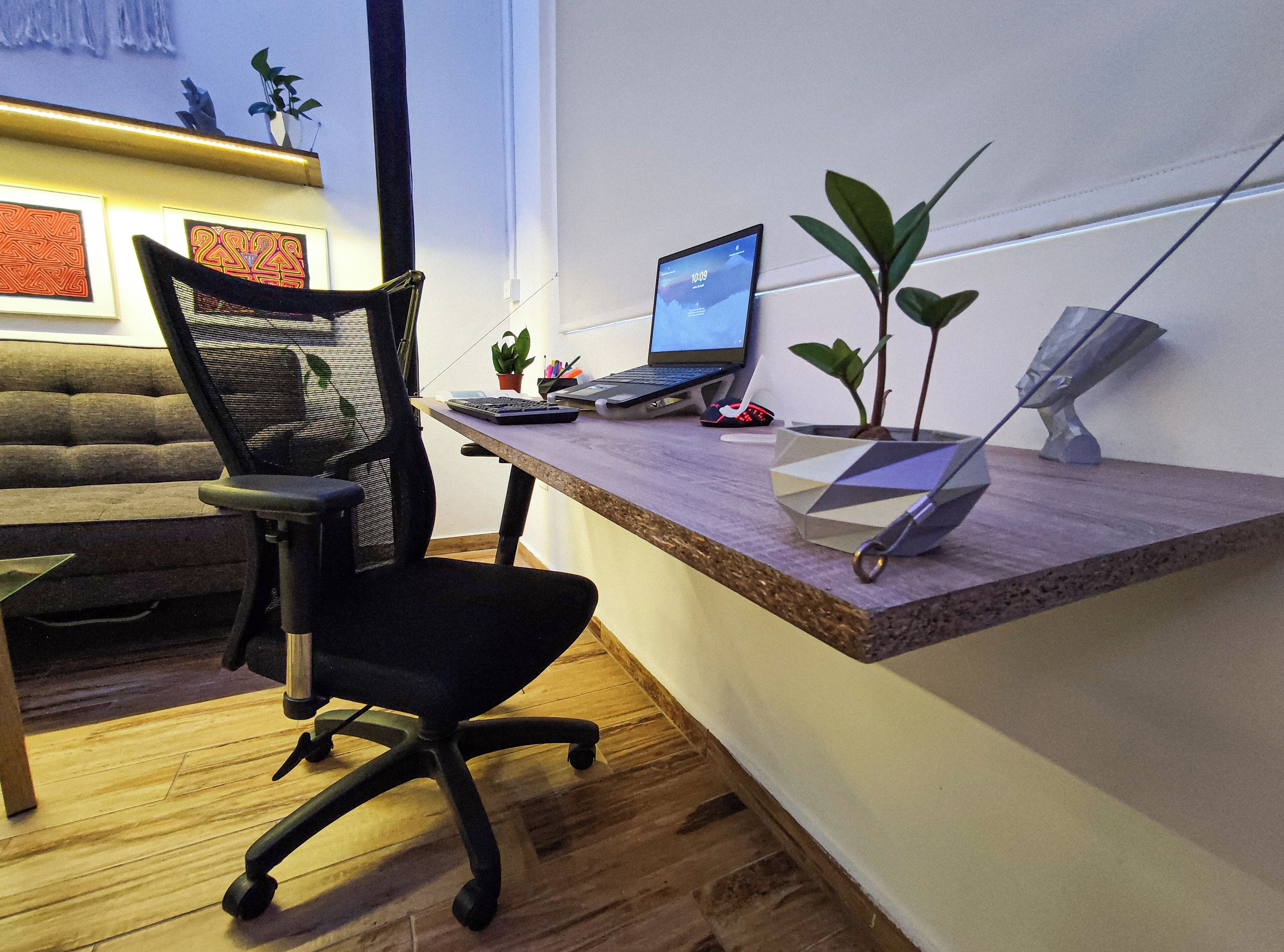 Un espacio de trabajo con escritorio, silla, ordenador portátil y plantas.