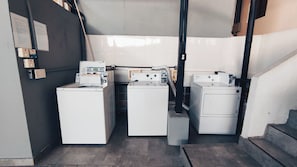 A laundry room with three stacked washers and dryers, a vent pipe, and a staircase leading to an upper level. - Mola Studio By Paradox (Panama City)