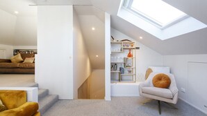A modern loft apartment with a skylight, a staircase, a living area with a sofa and armchair, and a built-in shelving unit. - Lilly`s Cottage - 3bdrm Heritage House, South Fremantle (South Fremantle)