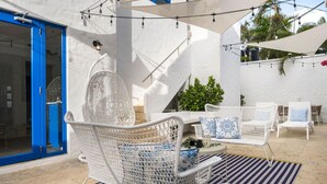 An outdoor seating area with white wicker furniture, a striped rug, and string lights.