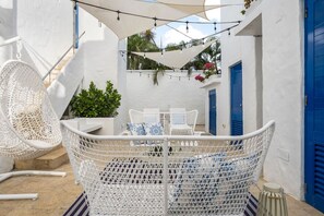 Una silla de mimbre blanca, un sofá de mimbre blanco y una mesita con cojines de estampado azul y blanco.