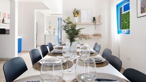 A dining area with a long table set for six, surrounded by black chairs. There is a vase with greenery on the table, and a framed map on the wall.