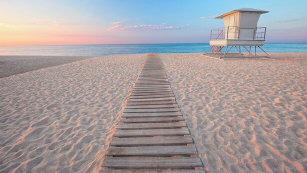 A wooden boardwalk leading to a lifeguard tower on a sandy beach.