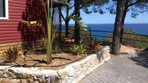 A red building with a stone retaining wall, tropical plants, and a view of the sea.