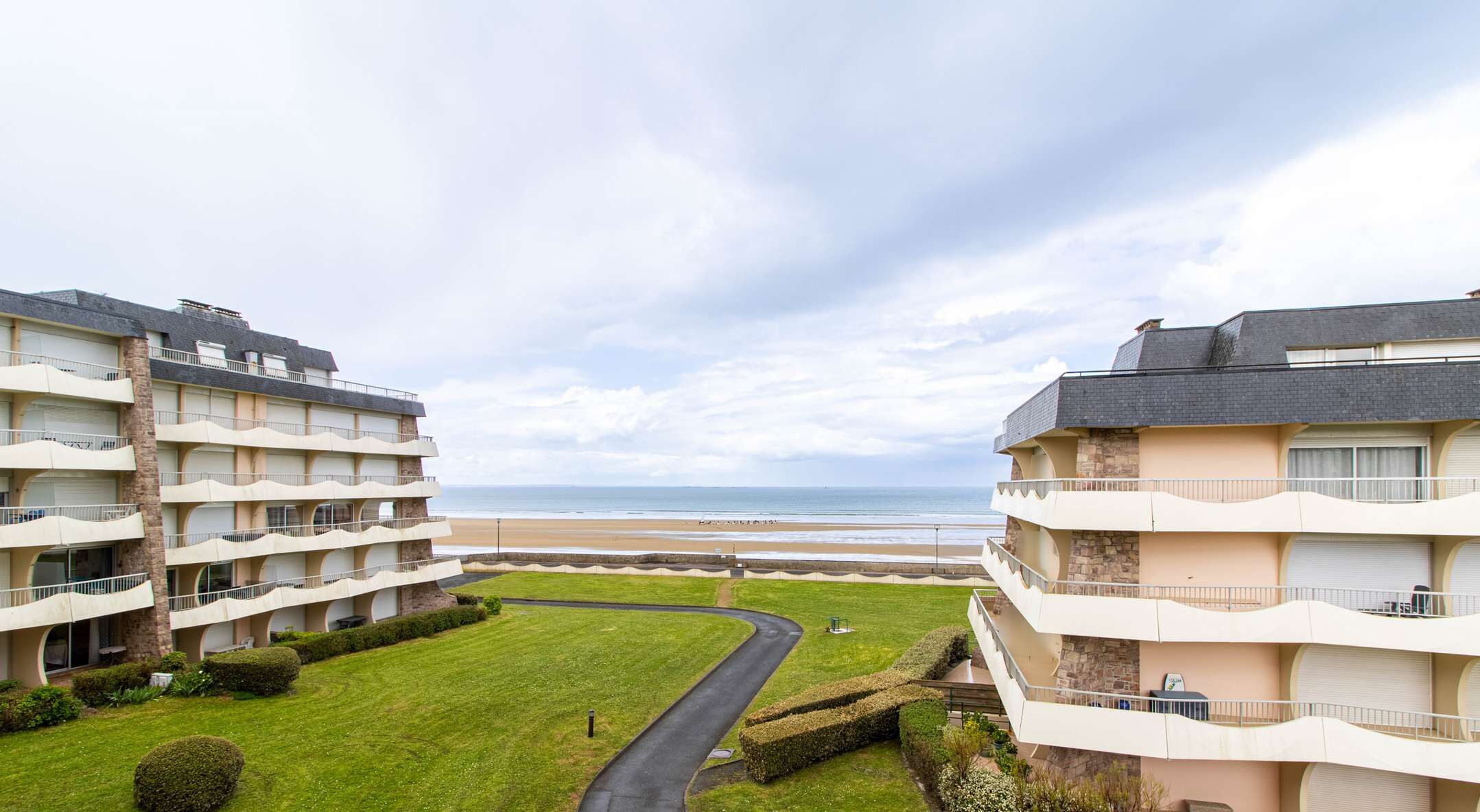 Un hôtel situé en bord de mer, doté de nombreux balcons, d’une allée sinueuse et d’une pelouse bien entretenue.