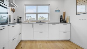 A modern kitchen with white cabinets, a wooden floor, a window with a view, and a coffee maker. - Stunning home in Holbæk with kitchen (Holbæk)