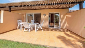 A covered patio with a table and chairs, a sliding glass door, and a tiled floor. - Apartement with air conditioning and pool (Pals)