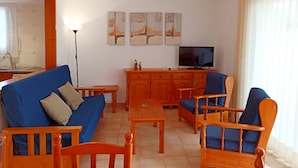 A living room with a blue sofa, wooden chairs, a wooden table, and a TV on a wooden cabinet. - Apartement with air conditioning and pool (Pals)