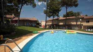 A swimming pool with a ladder, surrounded by buildings with tiled roofs and trees. - Apartement with air conditioning and pool (Pals)