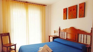 A bedroom with a wooden bed, a chair, a nightstand, and three paintings on the wall. - Apartement with air conditioning and pool (Pals)