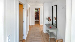 A hallway with a wooden floor, a rug, a bench, and a mirror on the wall.