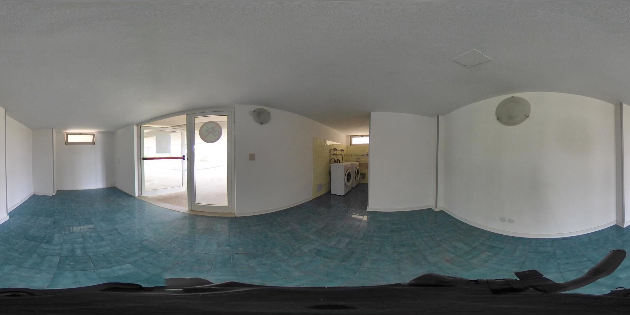 A spacious room with a blue-tiled floor, a door leading to a laundry area, and a window with a view.