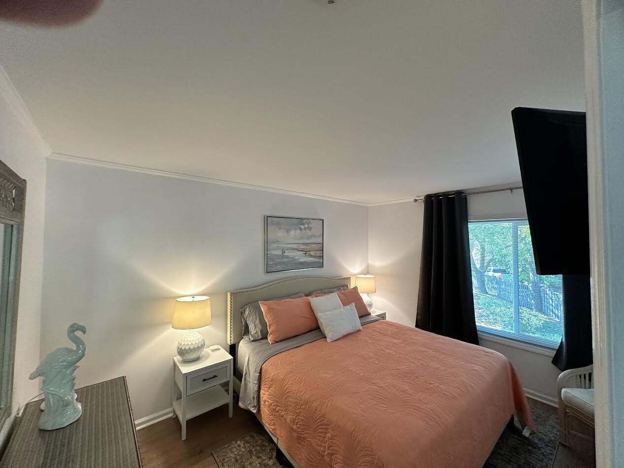 A bedroom with a bed, nightstands, a lamp, a window with curtains, and a wall-mounted picture.