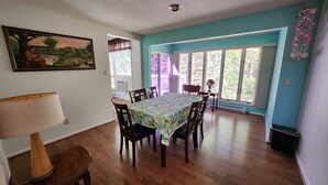 A dining room with a table set for four, wooden chairs, a painting on the wall, and a large window with a view of trees. - Three Bedroom House Lake George (Lake George)