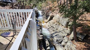A wooden deck with a white railing overlooking a rocky stream. - Three Bedroom House Lake George (Lake George)
