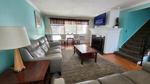 A living room with a sofa, coffee table, and chairs. There is a fireplace with a TV mounted above it. - Three Bedroom House Lake George (Lake George)