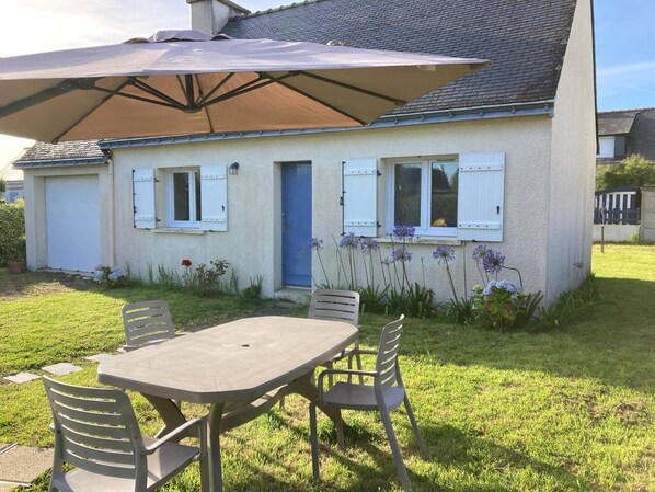 A house with a patio table and chairs, a blue door, and a large umbrella.