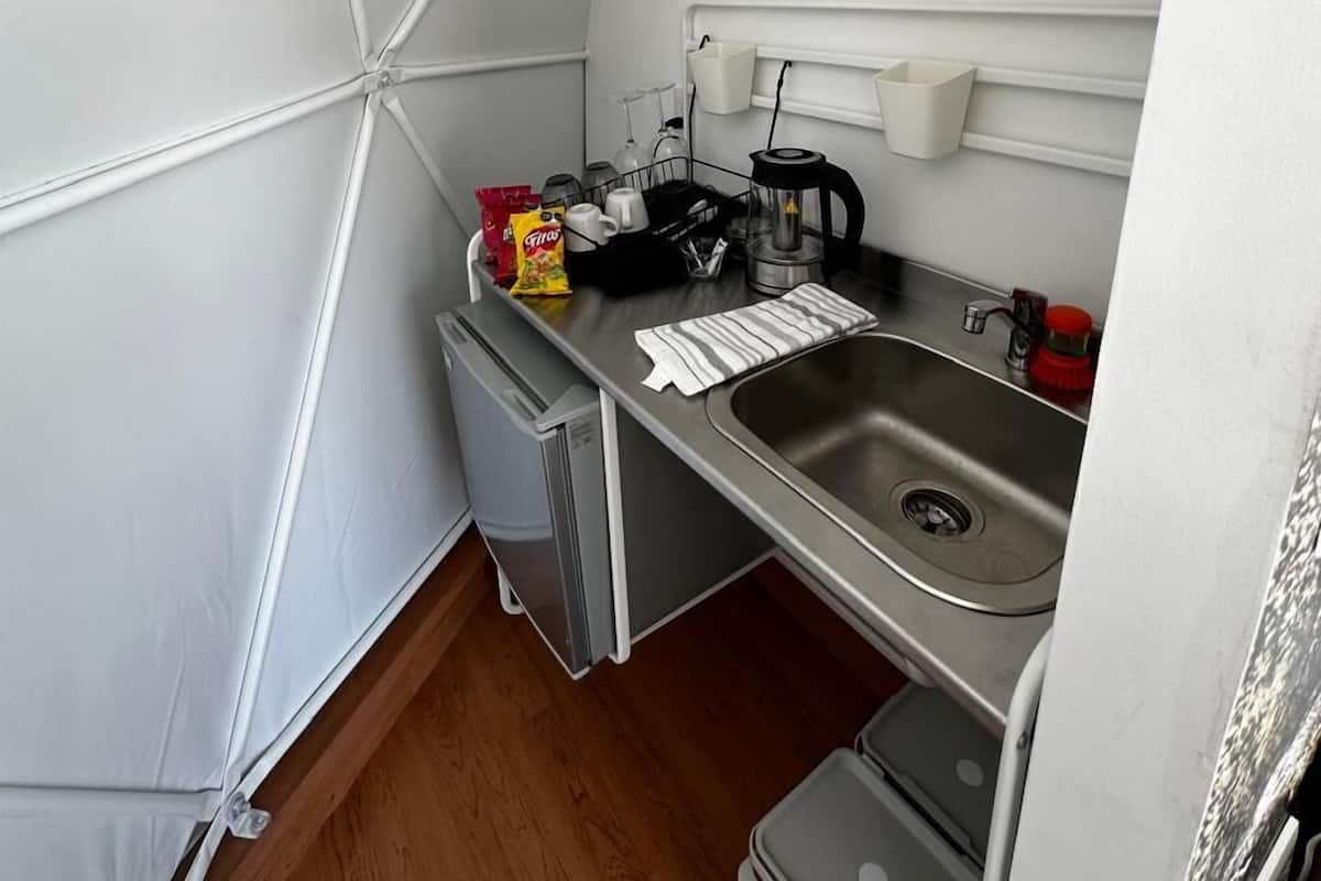 A compact kitchenette with a sink, a coffee maker, and a small trash bin.