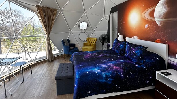A bedroom with a galaxy-themed bedspread, a round window, and a view of the outdoors. - ixkapada glamping  (Ixtapan de la Sal)