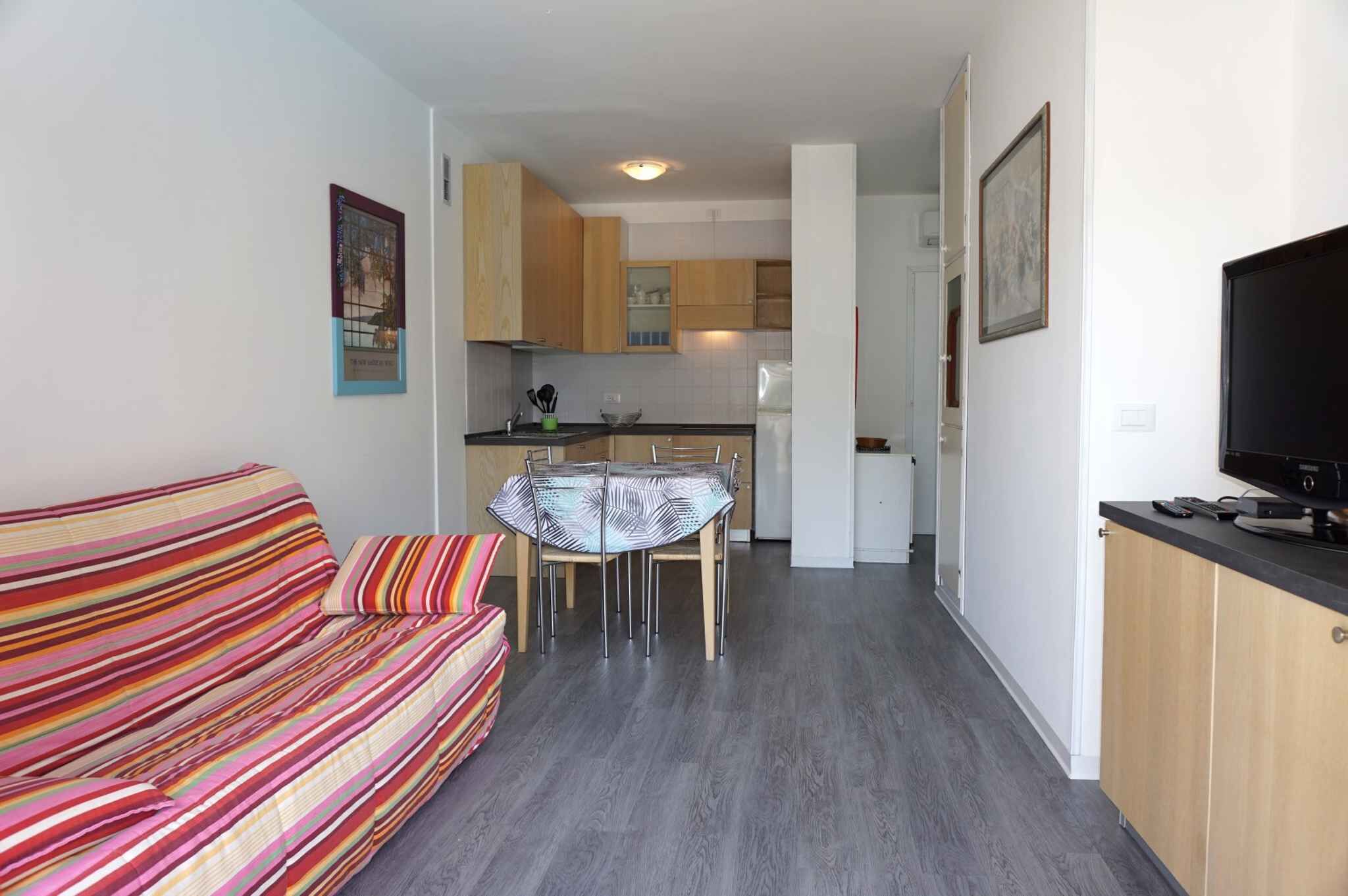 A compact living space with a striped sofa, a dining table with chairs, a kitchen area, and a television on a stand.
