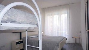 A bunk bed room with a desk and chair, a window with sheer curtains, and a door. - Holiday apartment with oceanfront pool (Porto Santa Margherita)