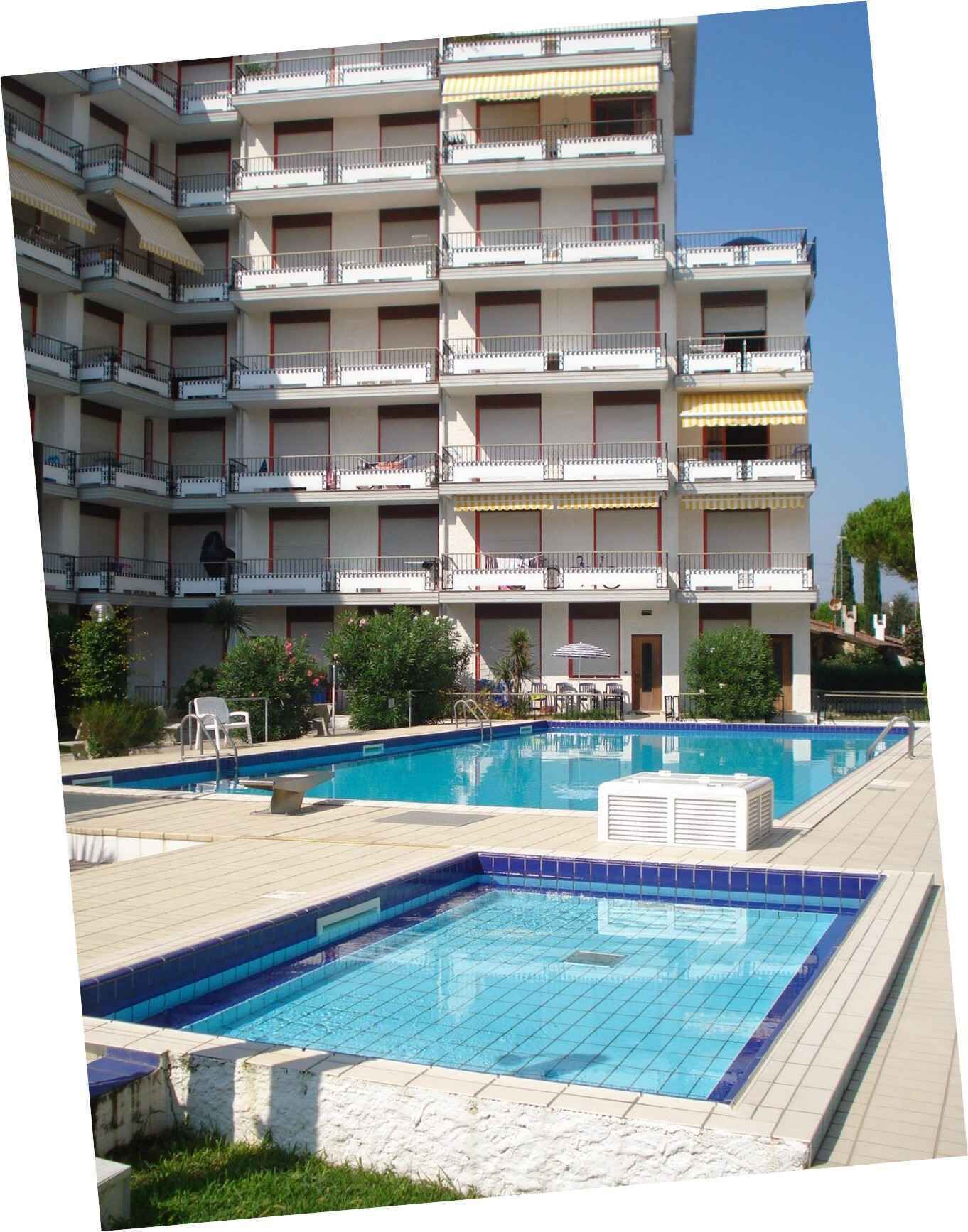 Un immeuble à plusieurs étages doté de balcons, d’une piscine et d’un espace extérieur aménagé pour s’asseoir.