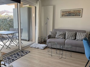 Een moderne woonkamer met een grijze bank, gestreepte kussens, een glazen salontafel, en een eethoek met een tafel en stoelen.