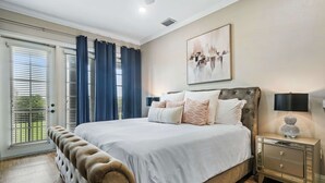 A bedroom with a large bed, a nightstand, a lamp, and a window with curtains.