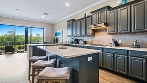A modern kitchen with dark cabinetry, a large island with stools, and a view of the outdoors.