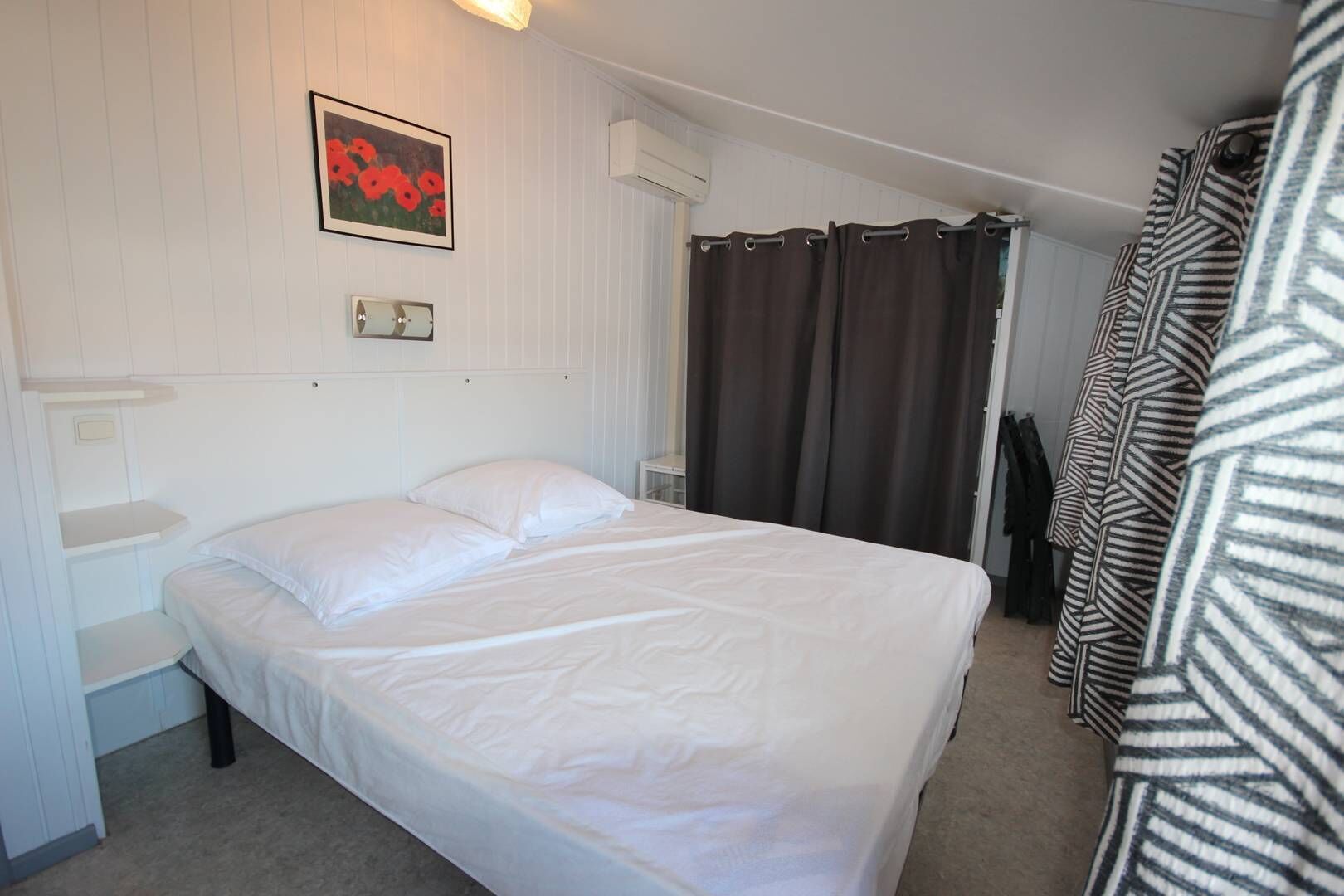 Una habitación de hotel con cama, espejo, cuadro enmarcado, ventana con cortinas y puerta.