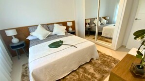 Une chambre d’hôtel avec un lit, des tables de chevet, un miroir et une plante.