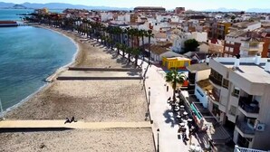 Une ville côtière dotée d’une plage de sable, d’une promenade bordée de palmiers et d’immeubles avec des balcons.