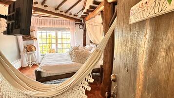 A rustic bedroom with a hammock, a bed with pillows, a TV, and a sign reading "Henriette".