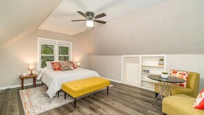 Ein Schlafzimmer mit einem Bett, einer gelben Bank, einem Deckenventilator, einem Fenster und einem kleinen Tisch mit Stuhl.