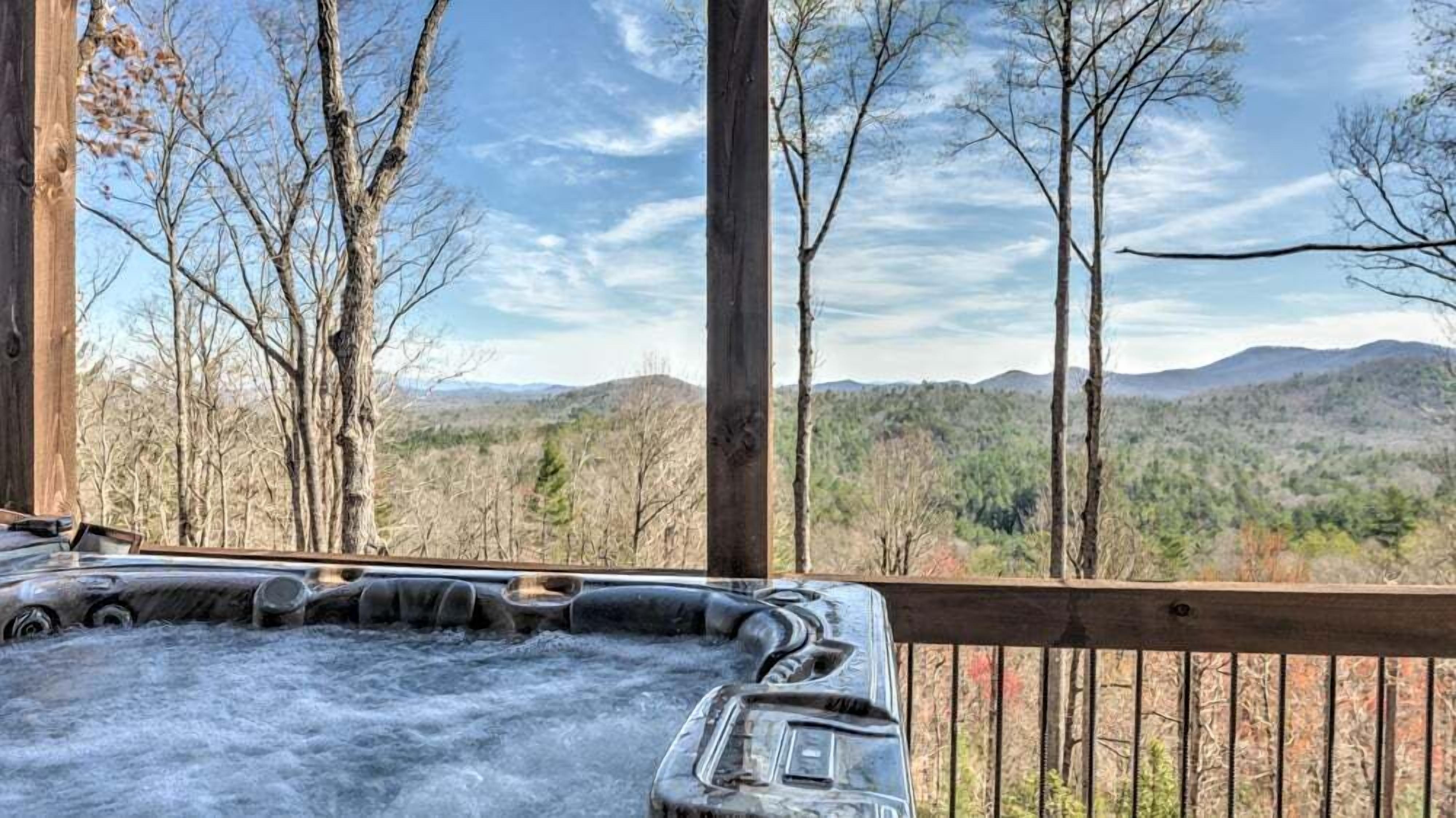 A hot tub on a wooden deck with a view of a forest and mountains.