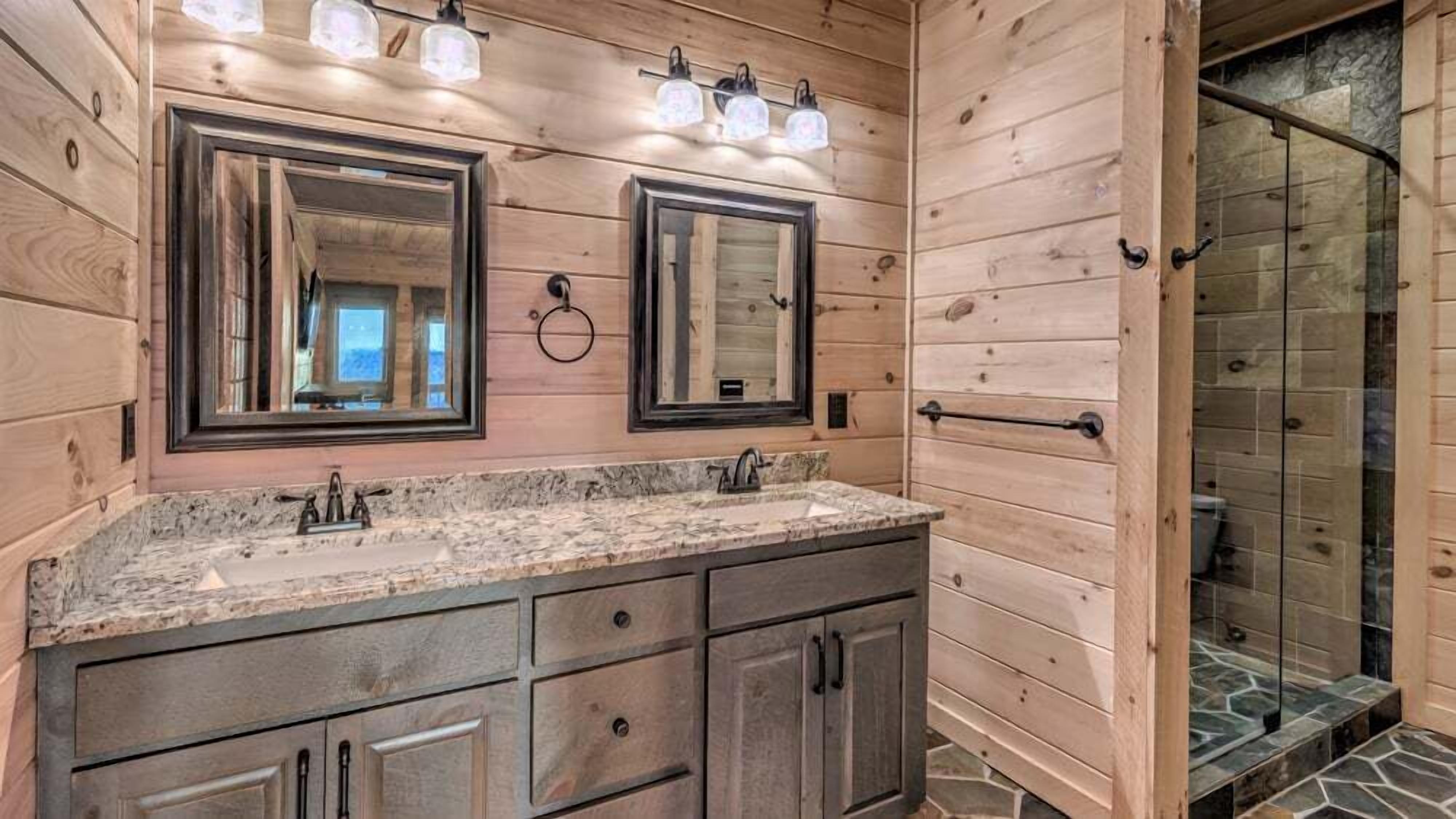 Un bagno in legno con due specchi, un piano di lavoro in granito e una doccia rivestita di piastrelle di pietra.