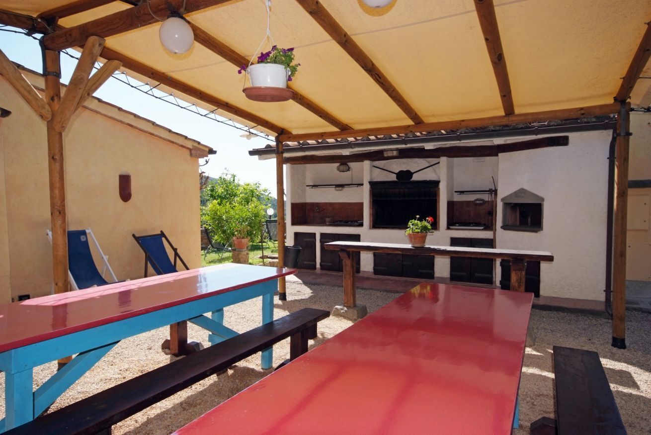 An outdoor patio area with a long red table, blue chairs, and a hanging plant.