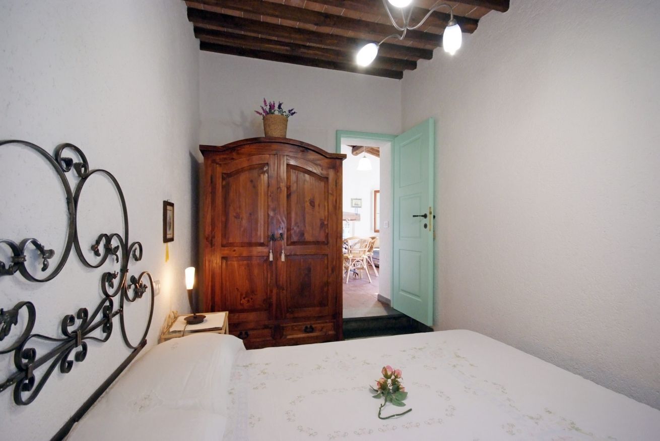 Une chambre avec une armoire en bois, un lit recouvert d’une couvre-lit à motifs floraux et une tête de lit en métal.