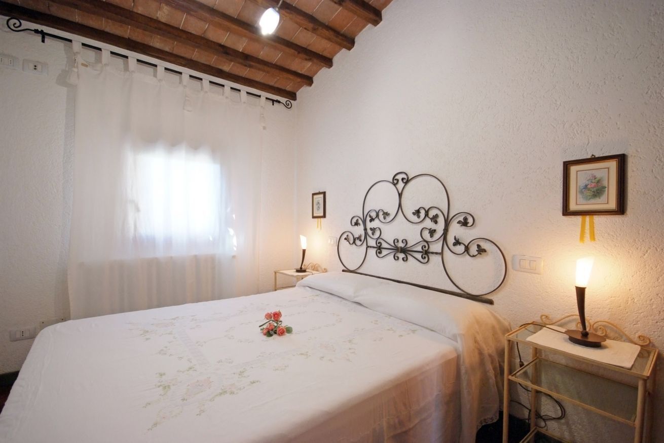 A bedroom with a bed, a nightstand, a wall-mounted metal headboard, and a window with curtains.